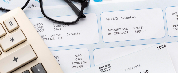 Close-up of payroll documents, paycheck stubs, calculator, and glasses on a desk, symbolizing payroll processing and financial accuracy using Gusto.