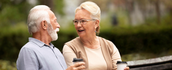 Smiling senior couple enjoying coffee on a park bench, reflecting comfort and connection supported by medical alerts and Senior Protection.