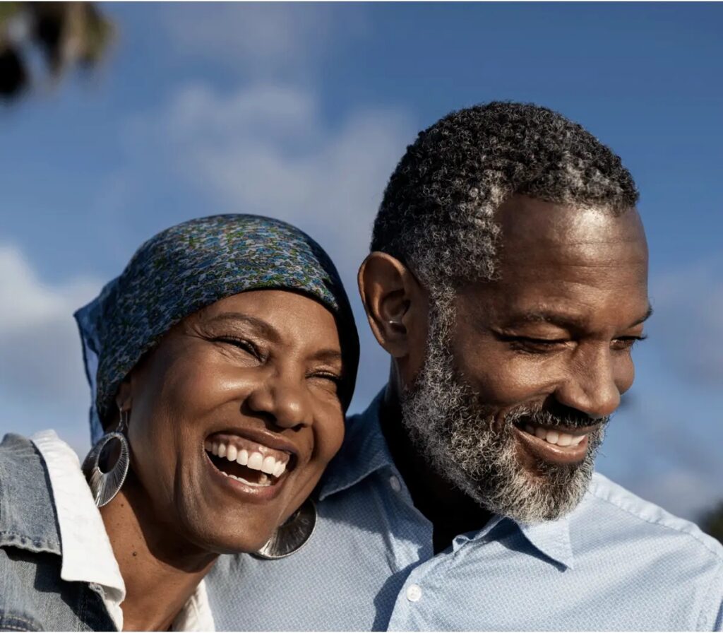 A smiling man wearing a virtually invisible Sony OTC hearing aid while laughing with a friend outdoors, showcasing the device's total discretion.