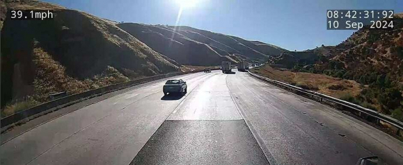 Wide angle SureCam dashcam image showing a multi lane highway through dry rolling hills with a car and two trucks driving ahead under bright morning sun. On screen overlays display speed at 39.1 mph and a timestamp of 08 42 31 on 10 Sep 2024 highlighting real time vehicle tracking data in motion.