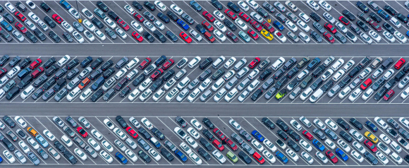 Aerial view of a large parking lot filled with rows of tightly parked cars in various colors, organized in neat lines across multiple lanes. The image highlights the scale and complexity of managing a vehicle fleet in a busy environment. It represents how RAM Tracking vehicle tracking solutions help monitor fleet movement, improve visibility, and optimize overall fleet performance.
