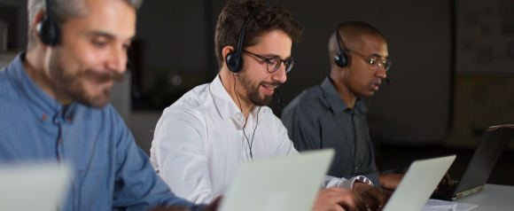 Customer support agents wearing headsets work on laptops in a call center environment, demonstrating how Ooma business phone systems powered by VoIP help teams manage customer calls and communication efficiently.