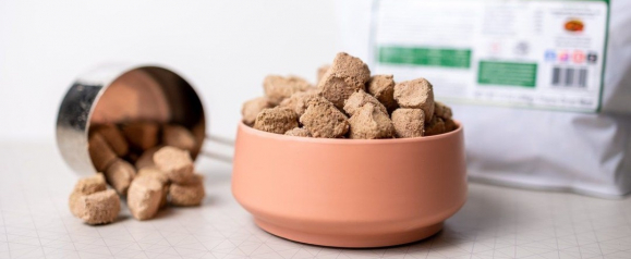 BARF World freeze-dried raw dog food nuggets served in a pink bowl with a measuring cup and product bag
