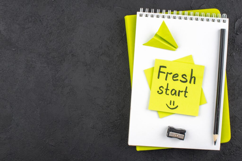 Spiral notebook and pencil on a dark desk with a yellow sticky note that reads "Fresh start". The visual represents the IRS Fresh Start Program and the opportunity for taxpayers to resolve tax debt and begin rebuilding their financial future.