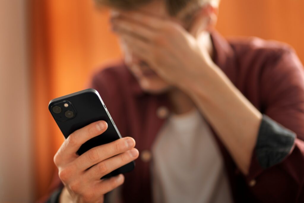 Person holding a smartphone and covering their face in distress after receiving a suspicious call, illustrating the fear and urgency commonly used in IRS Phone Call Scams. 