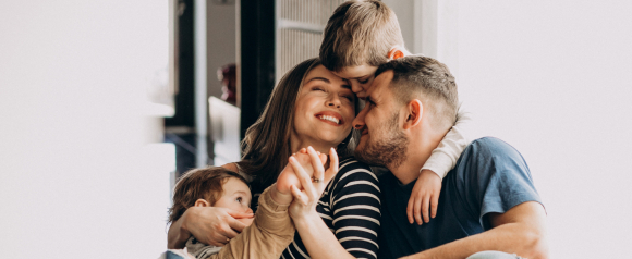 Parents smiling while their two young children hug them closely on a couch at home. Warm family moment representing protection and care with life insurance from SelectQuote.