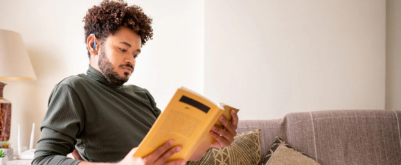 Person sitting on a couch reading a book while wearing a small Linner hearing aid, illustrating how Linner hearing aids provide discreet hearing support for everyday activities at home.
