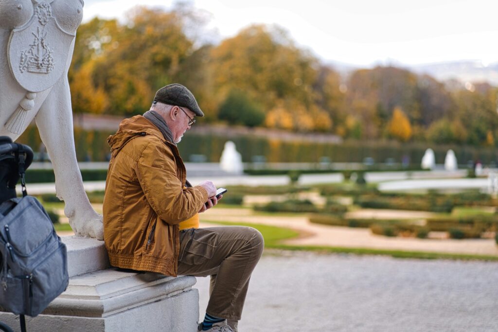 Older man sitting outdoors checking his phone, representing a retiree receiving a suspicious IRS tax scam message