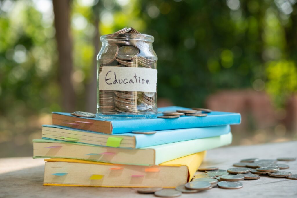 Glass jar labeled Education filled with coins sitting on a stack of books with loose change scattered around it representing savings and student loan relief options. The image highlights the cost of education and the importance of planning for federal student loan relief.