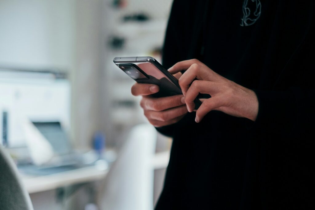 Person holding a smartphone and reading a message on the screen while standing indoors. The scene represents common tax scams where fraudulent messages attempt to impersonate the IRS to steal personal or financial information.
