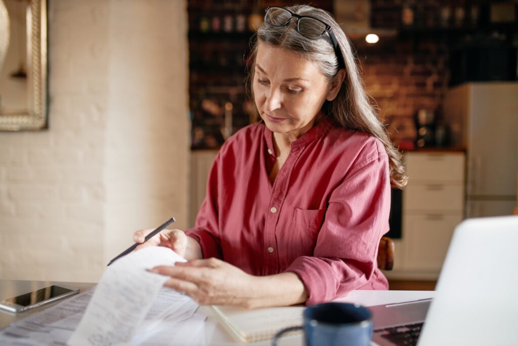 Middle-aged woman reviewing IRS tax transcript documents at home with a laptop and coffee