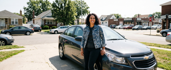 Smiling woman leaning against a gray sedan in a sunny suburban neighborhood street