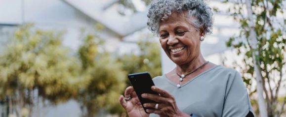 Smiling older woman with gray curly hair holding a Lively smartphone outdoors while staying connected with family