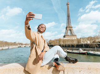 Smiling woman taking a selfie in front of the Eiffel Tower along the Seine in Paris.