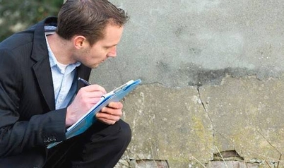 Insurance claims adjuster taking notes on a clipboard while inspecting a cracked exterior wall