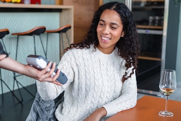 Smiling woman making a contactless payment with her smartphone at a card terminal in a cafe