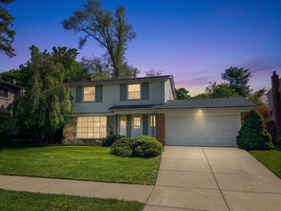 Two-story suburban home with an attached garage and landscaped lawn at dusk