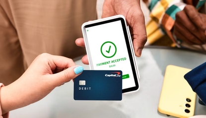 Person holding a Capital One debit card next to a payment terminal showing a payment accepted confirmation