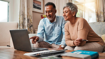 Older couple smiling while reviewing finances together on a laptop at home.