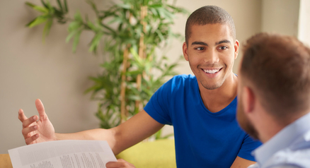 Smiling young man talking with a loan advisor who is holding a document during a financing consultation
