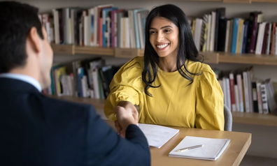 Smiling woman shaking hands with a loan officer across a desk after approving a financing agreement