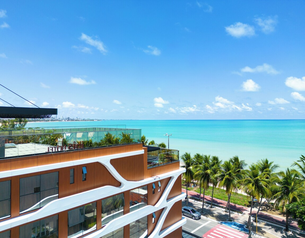 Modern beachfront hotel with a rooftop terrace overlooking a palm-lined avenue and turquoise sea.