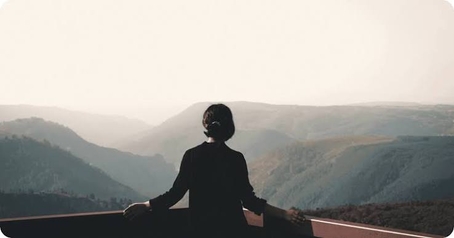 Silhouette of a person looking out over misty mountains from a viewpoint.