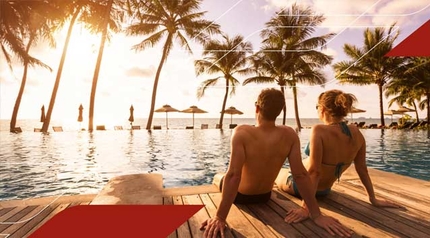 Couple relaxing by a tropical infinity pool at sunset surrounded by palm trees.