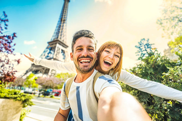 Happy couple taking a selfie in front of the Eiffel Tower in Paris.