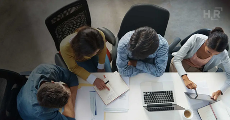 Overhead view of a team working together around a conference table with laptops, documents and notebooks.