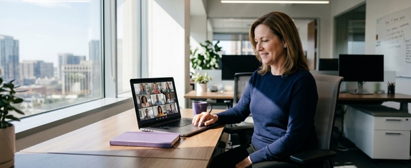 Smiling HR manager in navy sweater on a video call with a distributed remote team grid displayed on her laptop in a modern office