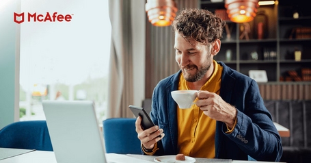Man drinking coffee while looking at his smartphone at a cafe table with the McAfee logo in the corner