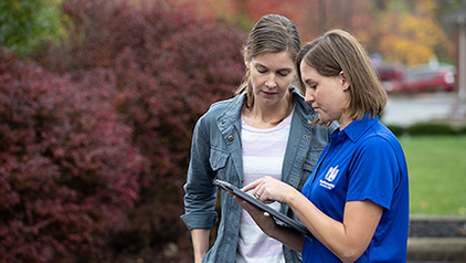 Nationwide's home insurance agent in a blue polo showing policy details on a tablet to a homeowner outdoors