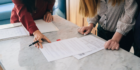 Two people reviewing printed documents on a marble counter, one holding a pen over the paperwork