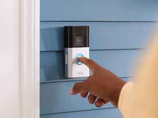 Finger pressing the illuminated button on a Ring video doorbell mounted on blue siding.