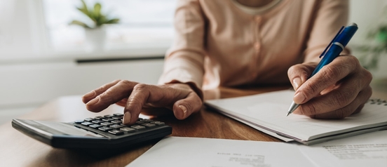 Person using a calculator and writing notes while reviewing mortgage paperwork at a desk