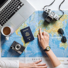 Overhead view of a person planning a trip on a world map with a passport, camera, laptop and coffee.