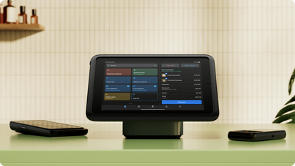 Shopify POS tablet on a retail counter displaying a customer checkout cart with itemized products and total, alongside card readers