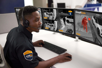 SimpliSafe monitoring agent reviewing home security camera feeds on multiple screens