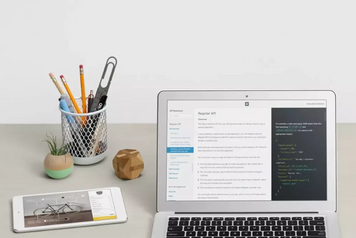 Square developer documentation for the Register API displayed on a laptop, with a tablet showing a point-of-sale screen on a desk with office supplies