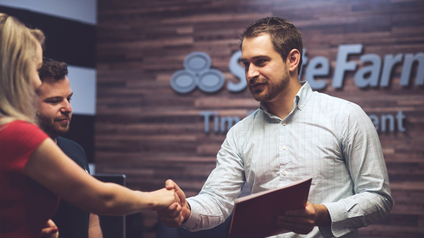 State Farm agent shaking hands with clients in front of a branded office wall