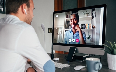 Man at a desk having a live video therapy session with a smiling counselor on his desktop monitor