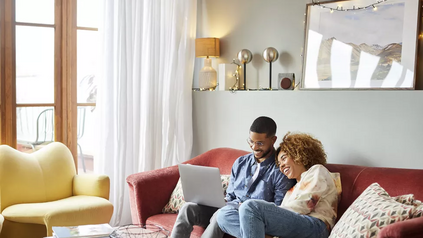Smiling couple sitting together on a couch at home looking at a laptop in a cozy living room