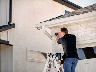 Technician on a ladder installing a Vivint outdoor security camera under a home's roofline