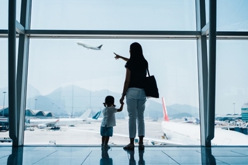 Mother and child watching a plane take off through an airport terminal window.